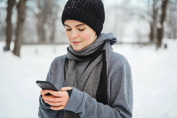 Kar Parkında Kış Antrenmanı Yaparken Akıllı Telefon Kullanan Atletik Kadın — Stok fotoğraf