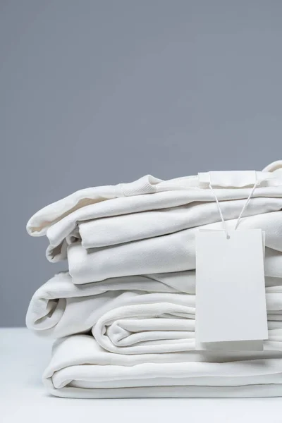 一堆堆新的白色衣服 灰色背景的空白服装标签 — 图库照片