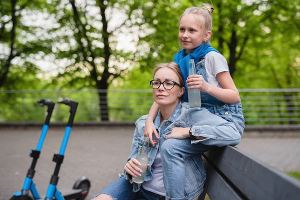 電気スクーターの幸せな母親と娘は市内公園でレモネードを飲んでいます — ストック写真