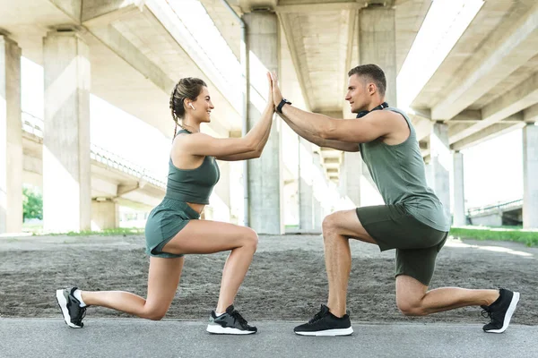 Athletic and happy couple during fitness training outdoors. Man and woman doing lunges during street workout.