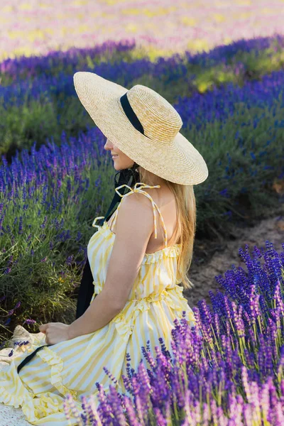 Όμορφη Νεαρή Γυναίκα Φορώντας Καπέλο Κάθεται Στο Χωράφι Γεμάτο Λουλούδια — Φωτογραφία Αρχείου