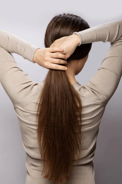 Молодая Женщина Показывает Свои Коричневые Здоровые Натуральные Волосы Сером Фоне — стоковое фото