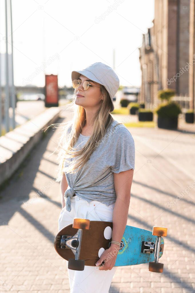Portrait of young stylish girl wearing panama hat with a longboard in a city