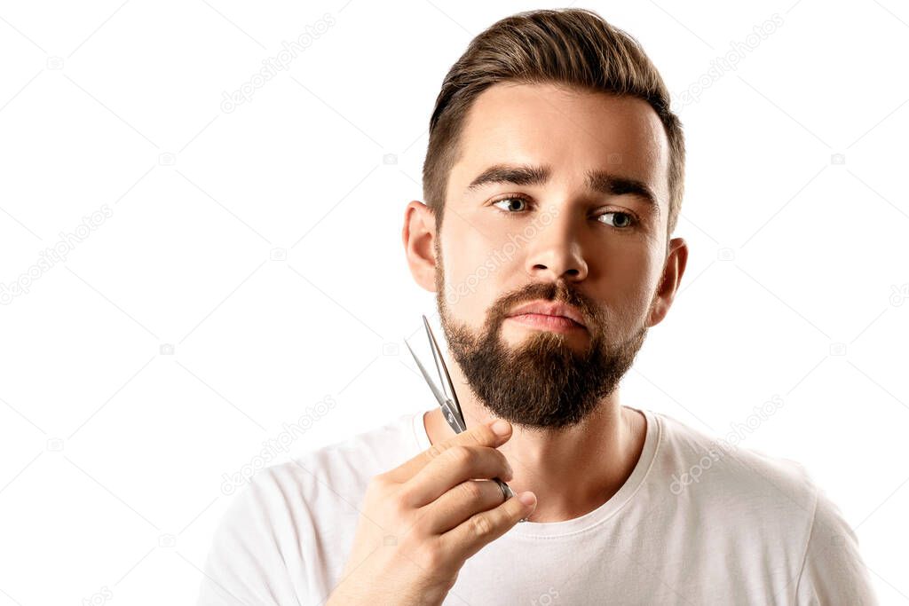 Handsome man trimming his beard with a scissors on white background