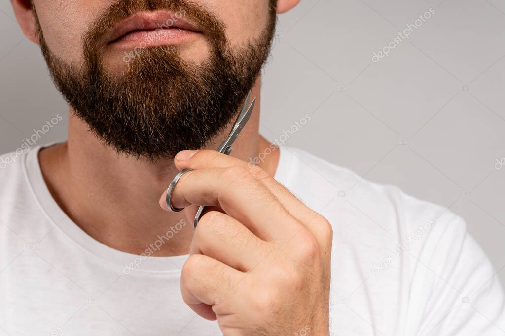 Well groomed man trimming his beard with a scissors 