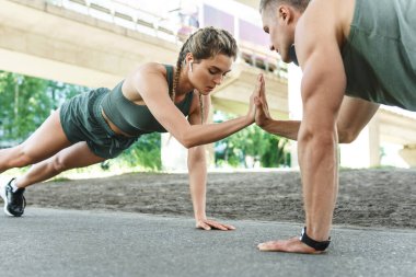 Atletik çift ve açık havada spor eğitimi. Erkek ve kadın, sokak egzersizi sırasında göğüs ve triseps kasları için şınav çekiyorlar. 