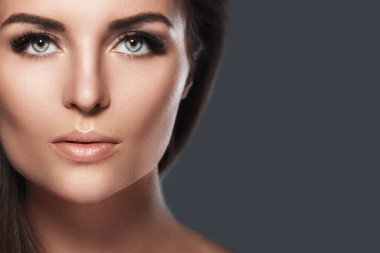 Koyu gri arka planda yapay kirpikleri olan genç ve güzel bir kadının portresi.