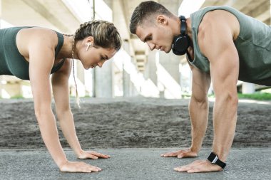 Atletik çift ve açık havada spor eğitimi. Erkek ve kadın, sokak egzersizi sırasında göğüs ve triseps kasları için şınav çekiyorlar. 