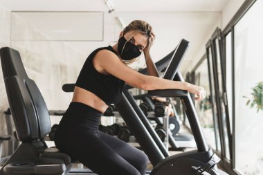 Yeni bir spor salonu. Spor yaparken koruyucu yüz maskesi takan genç bir atletik kadın..