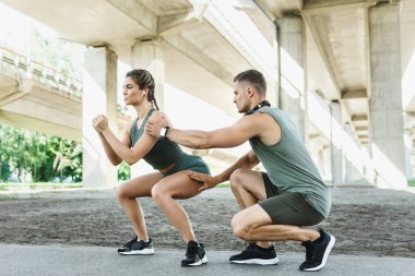 Atletik çift ve açık havada spor eğitimi. Kadın ve erkek sokak antrenmanı sırasında çömeliyor..