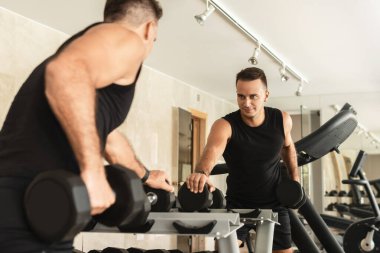 Spor salonunda vücut geliştirme egzersizi yaparken dambılla egzersiz yapan bir sporcu.