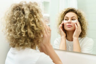 Banyoda cilt gençleştirmesi için göz altı bantları yapıştırılmış güzel bir kadın.