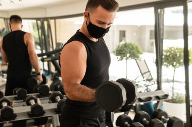 Yeni normal konsept. Spor salonundaki antrenmanı sırasında koruyucu yüz maskesi takan genç bir atletik..