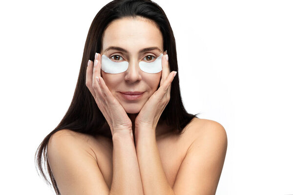 Anti aging treatment. Middle aged woman with applied sheet patches under her eyes on white background.