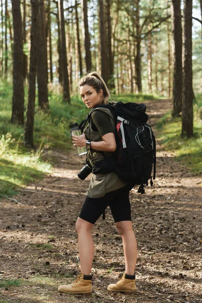 stock image Young female hiker with big backpack and reusable bottle for water in green forest