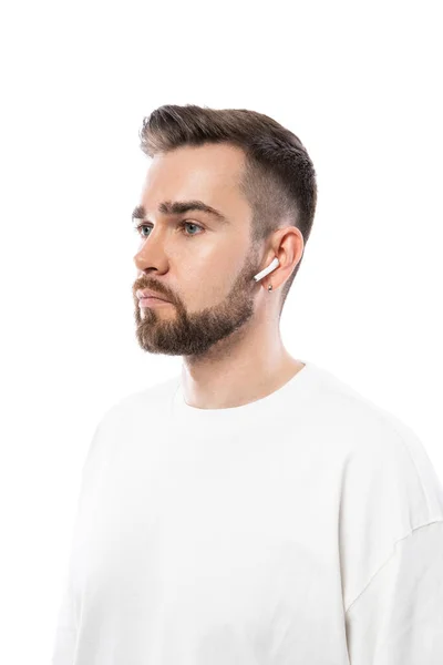 白い背景に無線イヤホンを使用した白い服のハンサムな髭の男の肖像画 — ストック写真