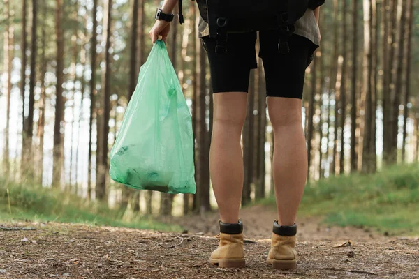 Young female hiker collecting plastic waste in green forest