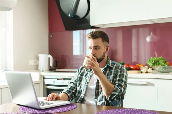 Junger Schöner Mann Trinkt Kaffee Oder Tee Und Benutzt Laptop — Stockfoto