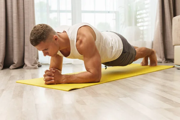 Young and muscular man doing plank during intense home workout