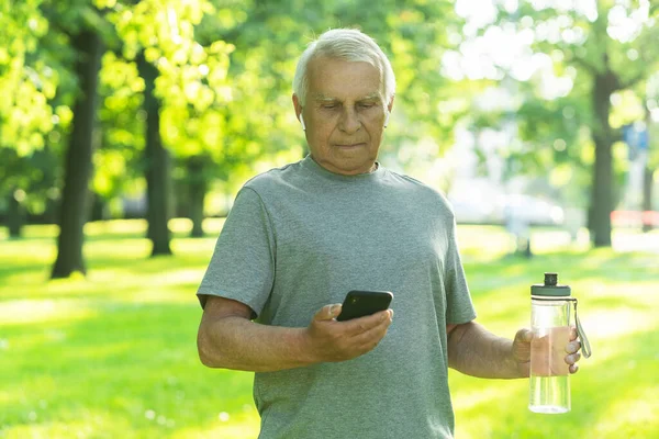 Feliz Anciano Activo Con Una Botella Agua Teléfono Inteligente Parque — Foto de Stock