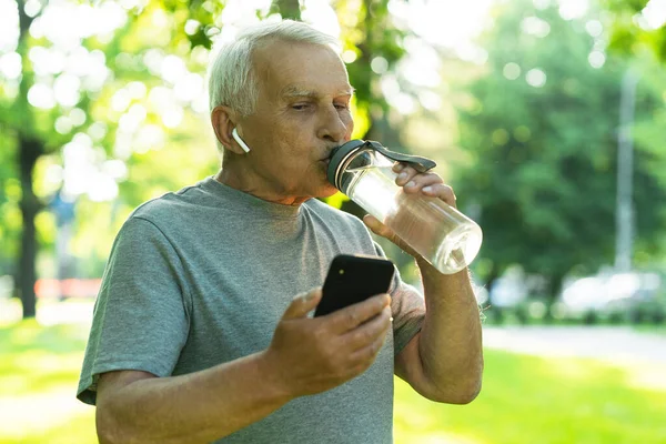 Feliz Anciano Activo Con Una Botella Agua Teléfono Inteligente Parque — Foto de Stock