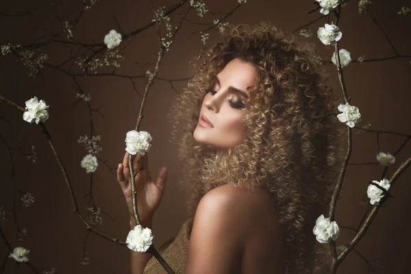 アフロの髪型と背景に白い花の多くと美しい化粧を持つ美しい若い女性の肖像画 — ストック写真