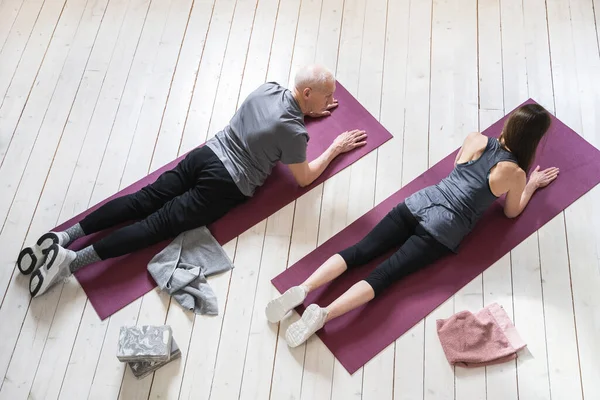 Two active elderly people working out on the exercise mats at home