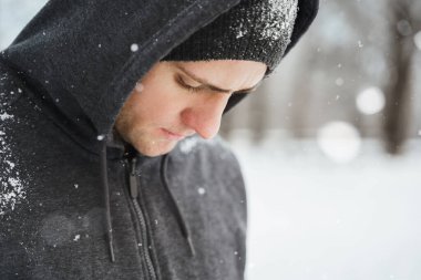 Karlı şehir parkında kış antrenmanı yaparken kapüşonlu giyen yakışıklı bir adamın portresi.