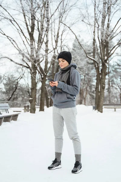Portret Młodej Sportowczyni Korzystającej Smartfona Podczas Zimowego Treningu Zaśnieżonym Parku — Zdjęcie stockowe
