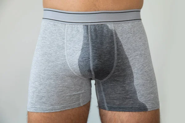 Man with wet briefs because of urinary incontinence on gray background