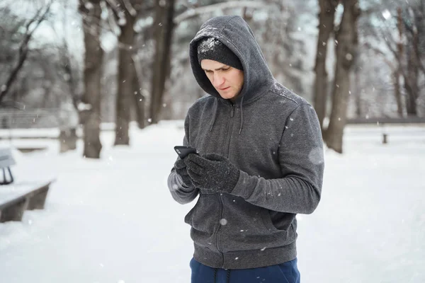 Jonge Sporter Met Smartphone Tijdens Wintertraining Besneeuwd Stadspark — Stockfoto