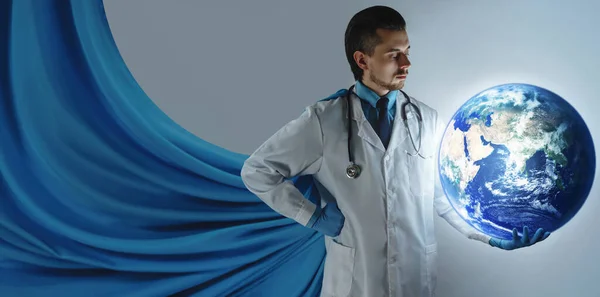 Brave doctor superhero  with blue cape holding planet earth in his hand. Concept of worldwide healthcare. Elements of this images furnished by NASA.