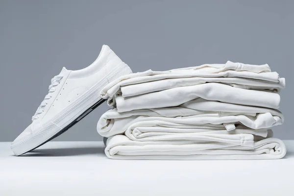 Στοίβα Από Λευκά Ρούχα Και Κομψούς Εκπαιδευτές Γκρι Φόντο — Φωτογραφία Αρχείου