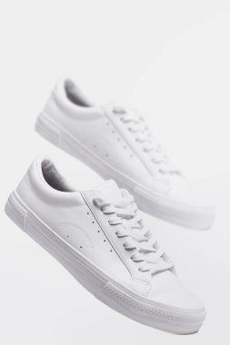 Gri arka planda bir çift beyaz deri spor ayakkabı.