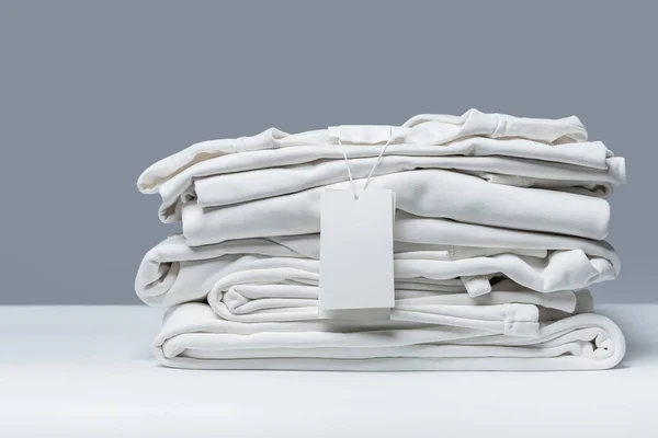 一堆堆新的白色衣服 灰色背景的空白服装标签 — 图库照片