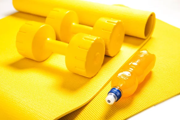 Close-up of yellow dumbbells, fitness mat and orange electrolyte drink