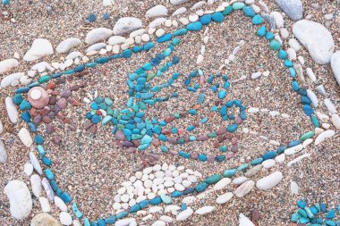 Bir kuşun çizimi deniz sahilinde çok renkli çakıl taşlarından yapılır. Yazın kıyıya yakın taşlar.