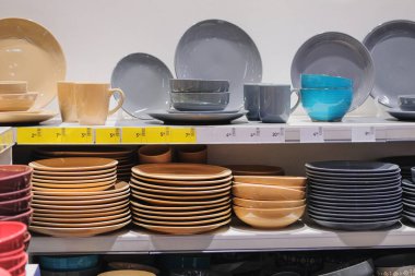 Bir süpermarkette raflardaki raflar için farklı gri ve bej bardaklar, kaseler ve tabaklar. Tabaklar dükkanda satılıyor..
