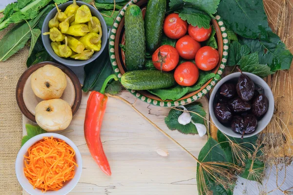 Various fermented vegetable food: cucumbers, tomatoes, apples, plums, peppers and carrots. Healthy food in bowls.