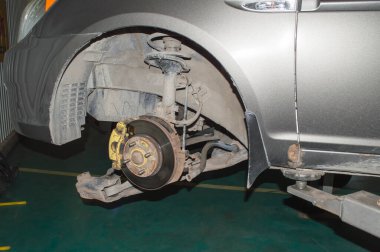 Sol ön tekerleği sökülmüş bir oto tamirhanesinde asansöre asılı gri bir arabanın ön süspansiyonu.