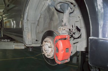 Kırmızı fren kalibreli gri bir arabanın ön sağ tekerleğinin askısı bir oto tamirhanesinde asansöre asılıydı.