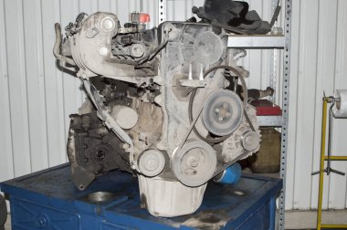 A view from the drive belt of the internal combustion engine and gearbox removed from the car and installed on a blue work table in the auto repair shop