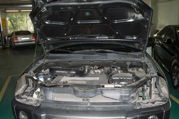 Front view of a car with an open hood and removed headlights that is in the auto repair shop