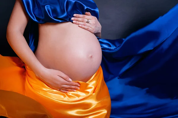 Pregnant Ukrainian woman. concept no war. stands wrapped in a cloth similar to the Ukrainian flag in the studio on a dark background. Ukrainian patriotism during the Russian military invasion of Ukrain
