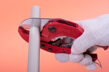 Tesisatçının elleri, turuncu bir sırt grubunda plastik bir boruyu makasla kesiyor.