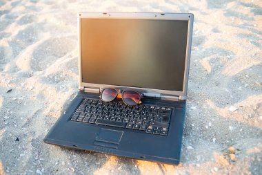 Kumsalda kumsalda dizüstü bilgisayar. Gözlükler güneşe karşı. Dinlenme ve rahatlama.