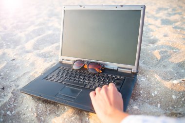 Kumsalda kumsalda dizüstü bilgisayar. Gözlükler güneşe karşı. Dinlenme ve rahatlama.
