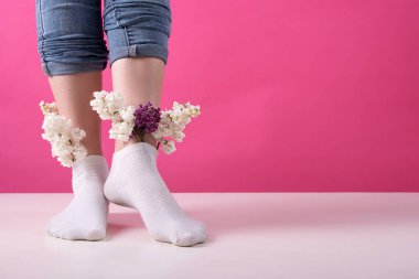 Pembe arka planda bir demet leylak çiçeği yerleştirilmiş çoraplı bir kızın bacakları. Kadın damarları ve bacakları kavramı