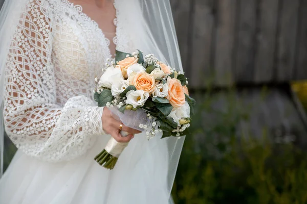 the bride in a white dress with sleeves holds a bouquet of bloom flowers in her hands. idea for event agencies wedding salon