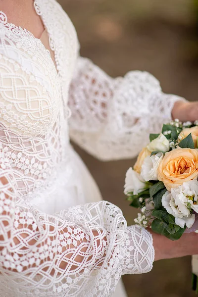 the bride in a white dress with sleeves holds a bouquet of bloom flowers in her hands. idea for event agencies wedding salon